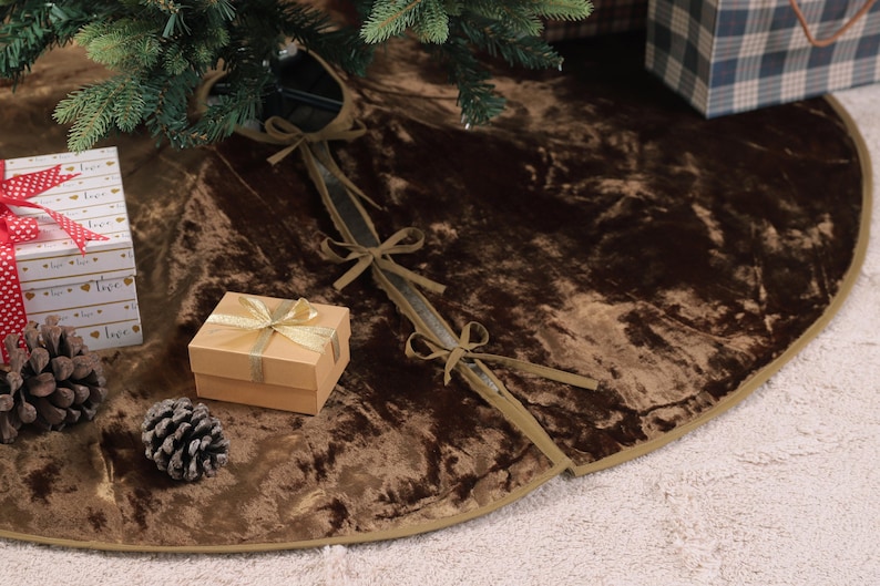 Puede incluir: Una falda de &aacute;rbol de Navidad de terciopelo marr&oacute;n con ribete dorado. La falda est&aacute; decorada con peque&ntilde;os regalos, pi&ntilde;as y una cinta. La falda est&aacute; dise&ntilde;ada para colocarse alrededor de la base de un &aacute;rbol de Navidad.
