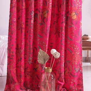 K&ouml;nnte beinhalten: Leuchtend pinke Vorh&auml;nge mit floralem Muster. Das detaillierte Design weist Farbt&ouml;ne von Orange, Gr&uuml;n und Braun auf. Eine klare Glasvase mit getrockneten dekorativen Stielen steht vor den Vorh&auml;ngen.