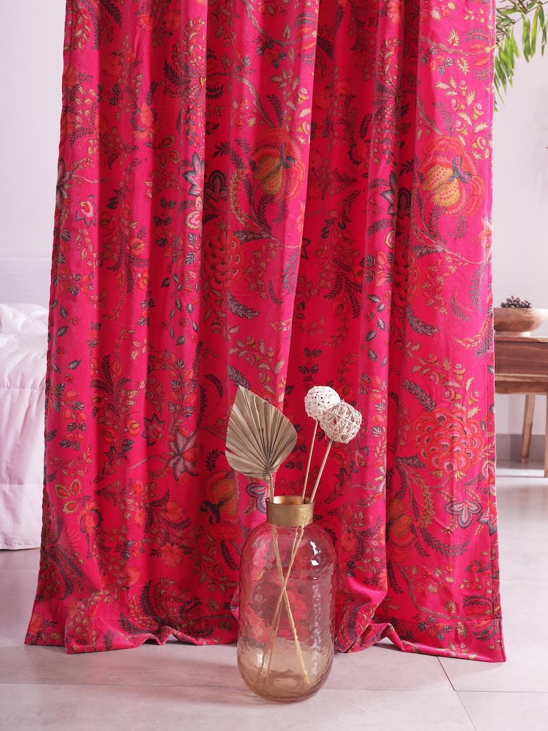 K&ouml;nnte beinhalten: Leuchtend pinke Vorh&auml;nge mit floralem Muster. Das detaillierte Design weist Farbt&ouml;ne von Orange, Gr&uuml;n und Braun auf. Eine klare Glasvase mit getrockneten dekorativen Stielen steht vor den Vorh&auml;ngen.