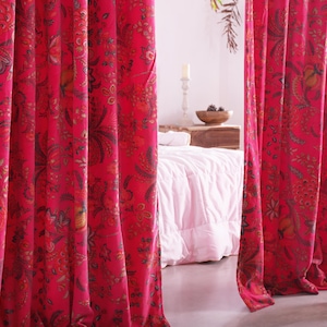 K&ouml;nnte beinhalten: Leuchtend rote Vorh&auml;nge mit floralem Muster. Die Vorh&auml;nge haben ein detailliertes Design mit Gelb-, Gr&uuml;n- und Braunt&ouml;nen. Sie h&auml;ngen vor einem Bett mit einer wei&szlig;en Bettdecke. Eine Vase mit dekorativen Elementen steht auf dem Boden.