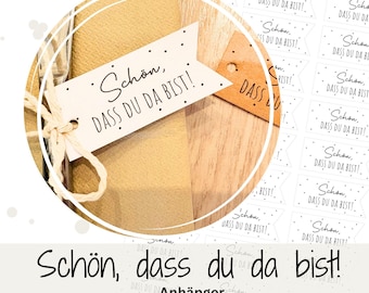 May include: A white printable tag with black text that reads "Schon, dass du da bist!"  The tag is attached to a piece of twine and is sitting on a wooden surface.  The tag is surrounded by other tags with the same text in a smaller size.