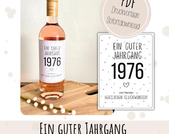 May include: A bottle of rosé wine with a label that reads "EIN GUTER JAHRGANG 1976." A matching card is displayed next to the bottle. The text on the card and bottle label is in black and white. The bottle has a gold cap.