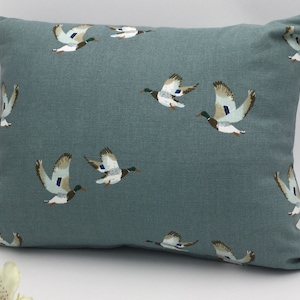 May include: A teal blue throw pillow with a pattern of flying ducks in shades of brown, green, and white.