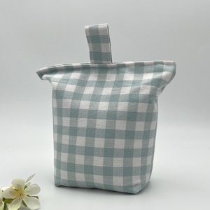 May include: A fabric doorstop featuring a light sage green and white gingham check pattern. The square-shaped object includes a matching fabric handle attached to the top centre, providing a functional grip for moving the weighted item.