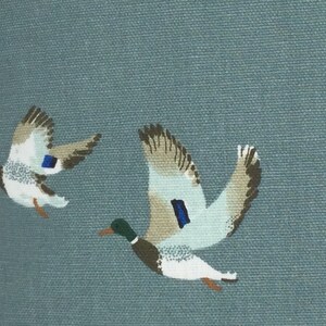 May include: A blue fabric with a pattern of flying ducks. The ducks are white with brown and gray markings. The fabric has a subtle texture.