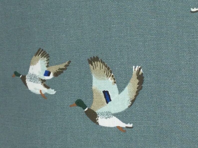 May include: A blue fabric with a pattern of flying ducks. The ducks are white with brown and gray markings. The fabric has a subtle texture.