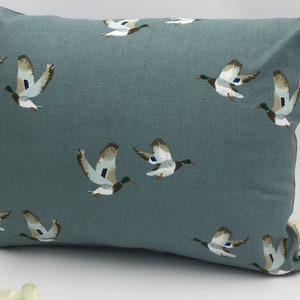 May include: A teal blue throw pillow with a repeating pattern of flying ducks. The ducks are brown, white, and green.