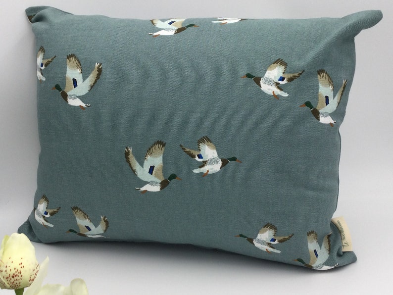 May include: A teal blue throw pillow with a repeating pattern of flying ducks. The ducks are brown, white, and green.