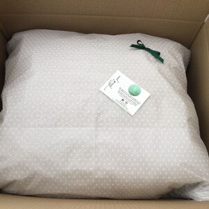 May include: A white tissue paper with small white dots, folded into a square shape, inside a brown cardboard box. A green ribbon is tied around the tissue paper. A small white card with the text "Thank you" and a logo is placed on top of the tissue paper.