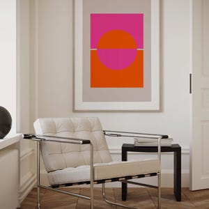 May include: A white leather armchair with a chrome frame sits in a room with a framed abstract print featuring a pink and orange circle design. The print is on a light gray background.
