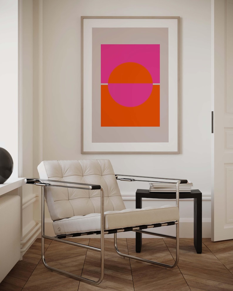 May include: A white leather armchair with a chrome frame sits in a room with a framed abstract print featuring a pink and orange circle design. The print is on a light gray background.