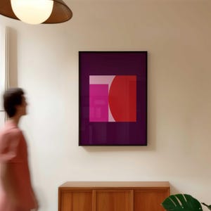 May include: A framed abstract art print featuring a geometric design. The artwork showcases a vibrant composition of a red semi-circle, a pink rectangle, and a light pink square, all set against a deep purple background. The frame is black.