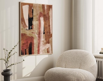 May include: Abstract art print in warm tones of brown, pink, and beige with black accents. The print is framed and hanging on a white wall above a white armchair.