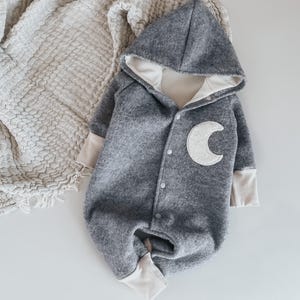 Könnte beinhalten: Grauer Baby-Strampler mit Kapuze und einem weißen Halbmond-Design. Der Strampler hat einen Reißverschluss und ist aus weichem, bequemem Stoff.