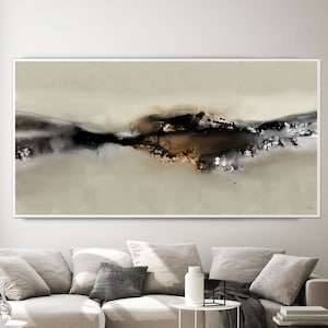 May include: Abstract art print with a beige background and a dark brown, black, and silver abstract design in the center. The print is framed in a white frame and is hanging on a white wall above a beige sectional sofa.