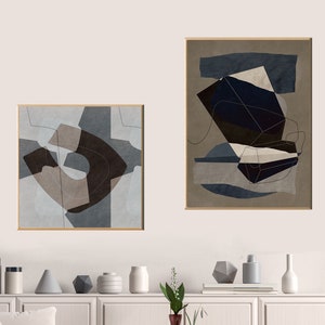 May include: Two abstract geometric art prints in brown, blue, and white frames. The prints are hanging on a white wall above a white cabinet with a white countertop. There are decorative vases and plants on the countertop.