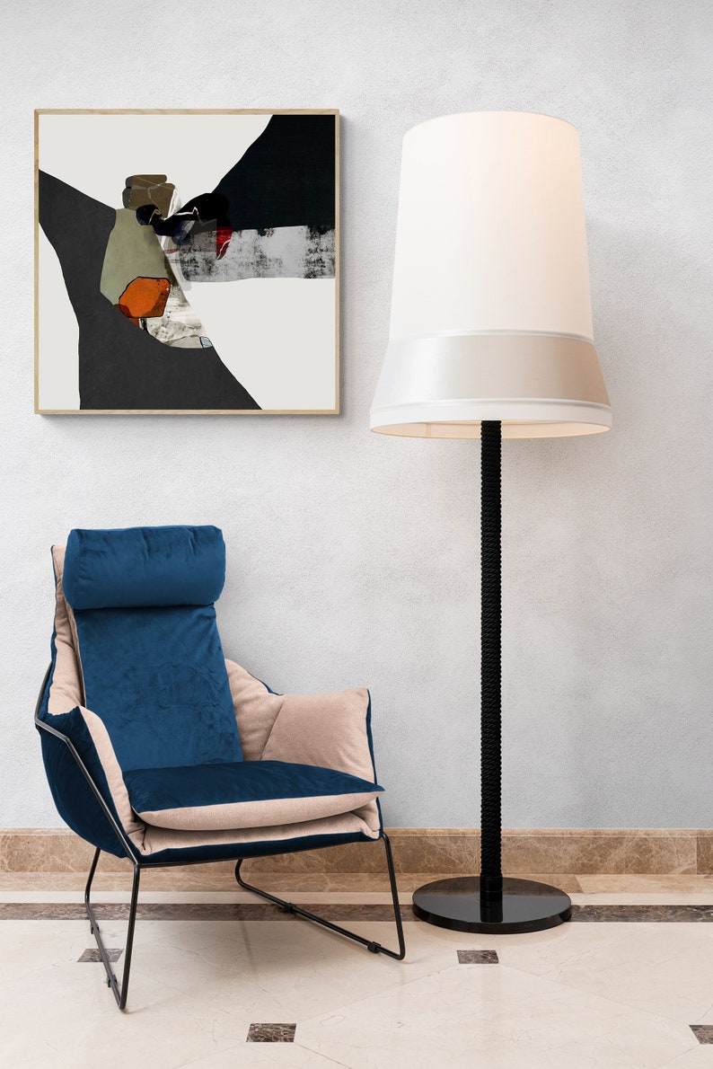 May include: A blue velvet armchair with a beige cushion sits in front of a white wall with a framed abstract painting and a tall black floor lamp with a white lampshade.