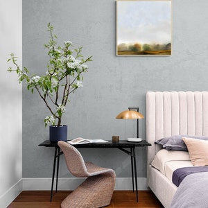 Op de afbeelding: Een slaapkamerinterieur met een wit hoofdeinde, een zwart bureau met een gevlochten stoel, een plant in een pot met witte bloemen en een ingelijst landschapsschilderij aan de muur.