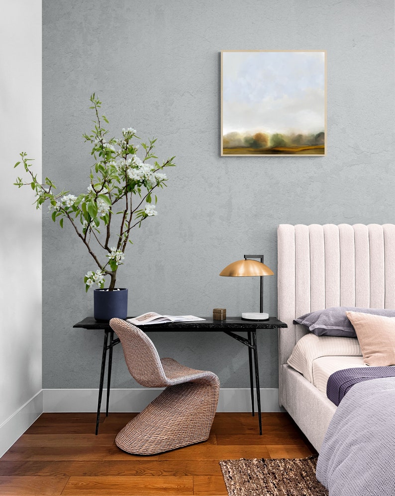 Op de afbeelding: Een slaapkamerinterieur met een wit hoofdeinde, een zwart bureau met een gevlochten stoel, een plant in een pot met witte bloemen en een ingelijst landschapsschilderij aan de muur.