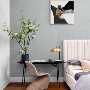May include: A bedroom interior with a white headboard, a black desk with a woven chair, a lamp with a gold shade, and a framed abstract painting on the wall. A potted flowering tree is in the corner of the room.
