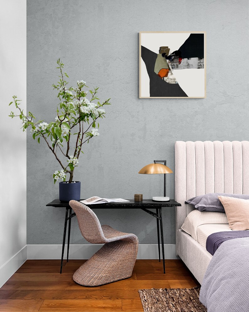 May include: A bedroom interior with a white headboard, a black desk with a woven chair, a lamp with a gold shade, and a framed abstract painting on the wall. A potted flowering tree is in the corner of the room.