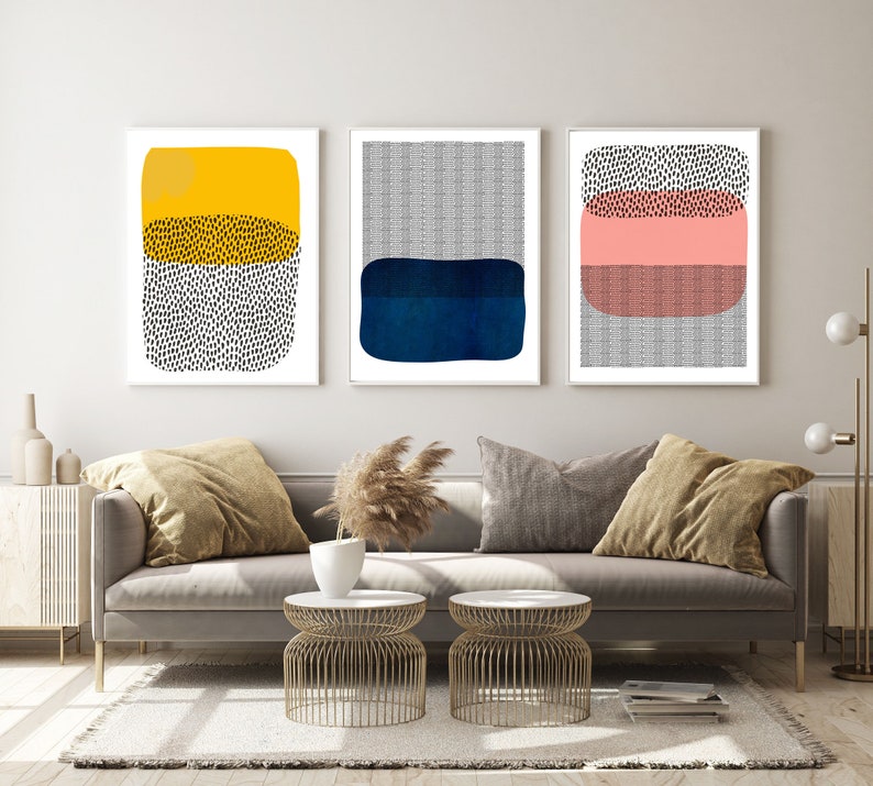 May include: Three framed abstract art prints. Each print features a rectangular shape with layered colors and textures. One print has yellow, black, and white elements. Another has gray and blue. The third print has pink, gray, and black.