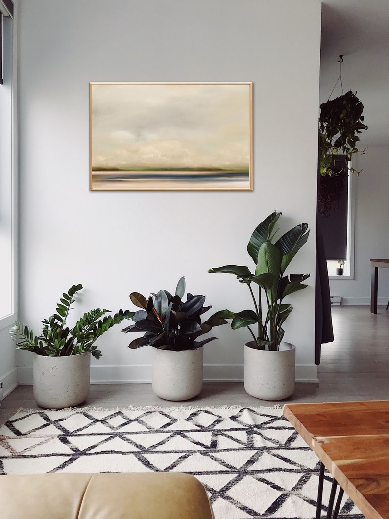 May include: A minimalist living room with a framed abstract landscape painting on the wall, three potted plants, a patterned rug, and a wooden coffee table.