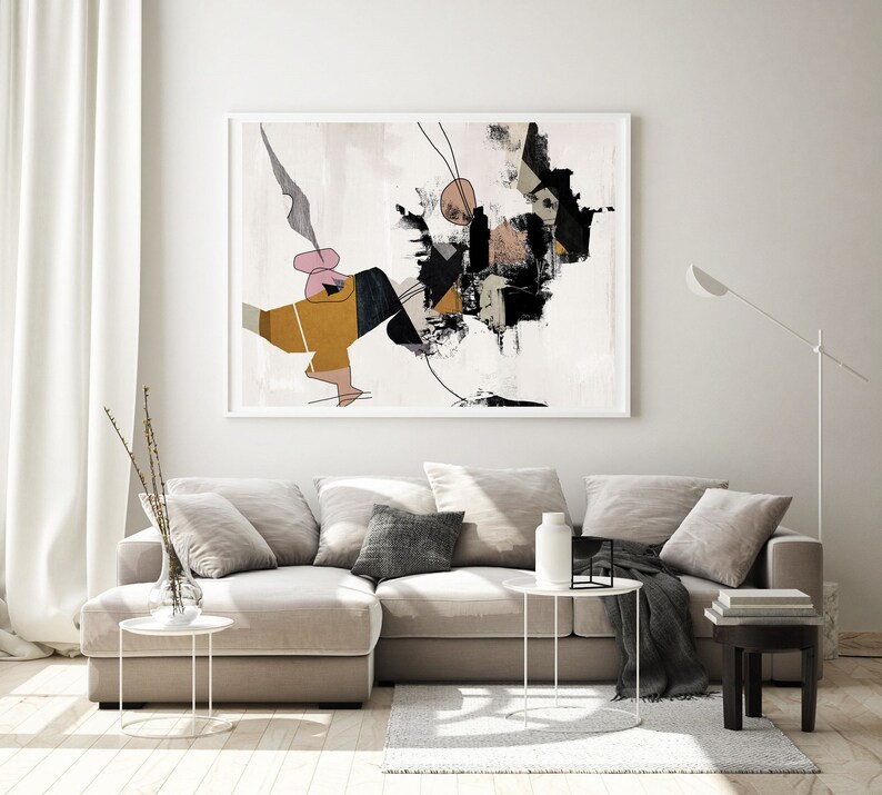 May include: Abstract art print in black, white, brown, and pink colors. The print features geometric shapes and lines on a white background. The print is framed in a white frame and is hanging on a white wall above a beige sectional sofa.