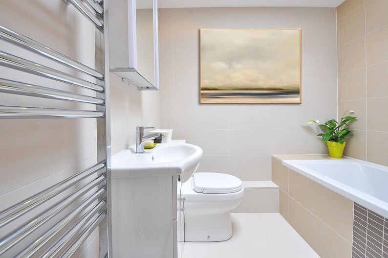 May include: A white bathroom with a white toilet, a white sink, a chrome towel rack, a bathtub, and a framed abstract landscape painting on the wall.