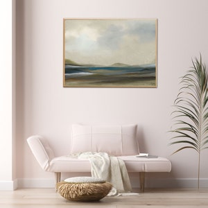 K&ouml;nnte beinhalten: Ein gerahmtes abstraktes Landschaftsbild in gedeckten T&ouml;nen von Blau, Gr&uuml;n und Braun. Das Bild zeigt eine ferne K&uuml;ste mit einem Gew&auml;sser im Vordergrund. Das Bild h&auml;ngt an einer wei&szlig;en Wand in einem Wohnzimmer.