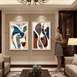 May include: Two framed abstract art prints. The artwork features a mix of shapes and colors, including blue, orange, brown, and beige. The prints are displayed in a living room setting with neutral-toned walls and furniture.