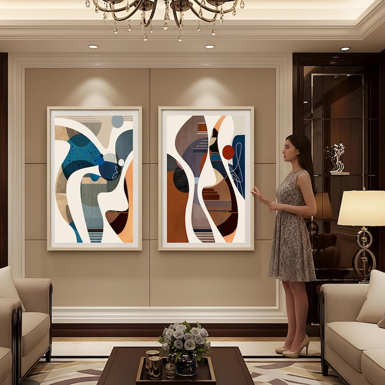 May include: Two framed abstract art prints. The artwork features a mix of shapes and colors, including blue, orange, brown, and beige. The prints are displayed in a living room setting with neutral-toned walls and furniture.