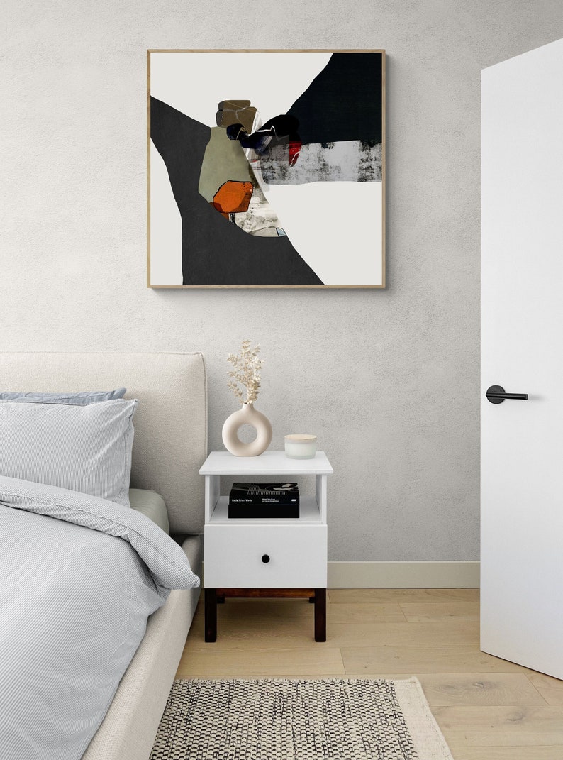 May include: White nightstand with a single drawer and an open shelf. The nightstand has a dark wood base and a white top. A book, a small vase with dried flowers, and a white candle are on the top shelf. The nightstand is in a bedroom with a white bed and a white door.