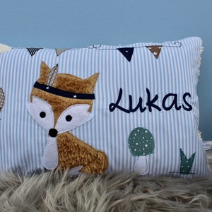 May include: A blue and white striped pillow with a brown fox wearing a blue headband with white stars. The pillow also has a mushroom, a green leaf, and the name "Lukas" embroidered on it.