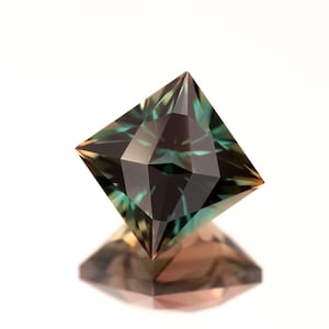 May include: A square-shaped gemstone with a dark green and brown color. The gemstone is cut into a pyramid shape with a pointed top and a flat base. The gemstone is reflecting light, creating a sparkling effect.