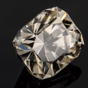 May include: A clear, faceted gemstone with a slightly yellowish hue. The gemstone is cut in a rectangular shape with many facets.