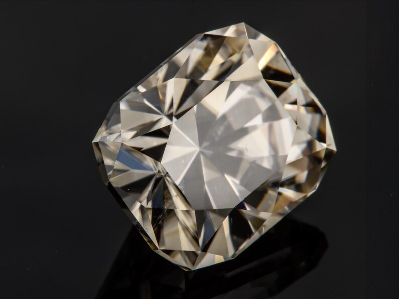 May include: A clear, faceted gemstone with a slightly yellowish hue. The gemstone is cut in a rectangular shape with many facets.