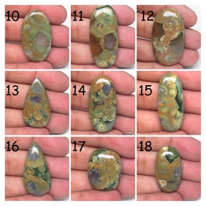 May include: Nine oval and teardrop shaped green, brown, and gray jasper cabochons with a polished finish. The cabochons are numbered 10 through 18.