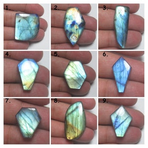 May include: Nine iridescent labradorite gemstones of various shapes and sizes, including oval, teardrop, and kite shapes. The stones have a blue-green base with flashes of gold and silver.