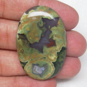 May include: Oval shaped green, brown, and white agate cabochon with a swirling pattern. The stone has a polished finish.