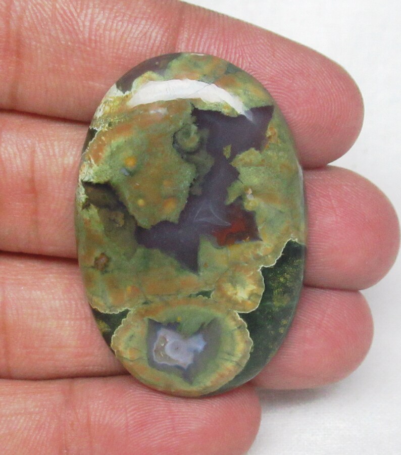 May include: Oval shaped green, brown, and white agate cabochon with a swirling pattern. The stone has a polished finish.