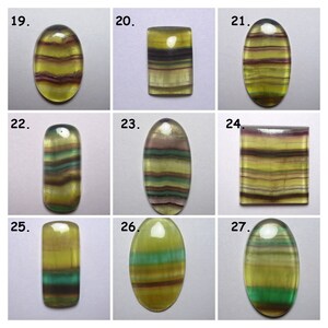 Puede incluir: Nueve piedras preciosas de fluorita talladas en cabuj&oacute;n con varios patrones de bandas de colores, incluyendo verde, amarillo, morado y marr&oacute;n. Las piedras est&aacute;n dispuestas en una cuadr&iacute;cula con los n&uacute;meros del 19 al 27.