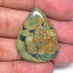 May include: A teardrop-shaped green, orange, and white gemstone cabochon with a mottled pattern.