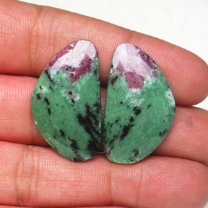Könnte beinhalten: Zwei grüne, rosafarbene und schwarze Edelsteinkabochons in Tropfenform.