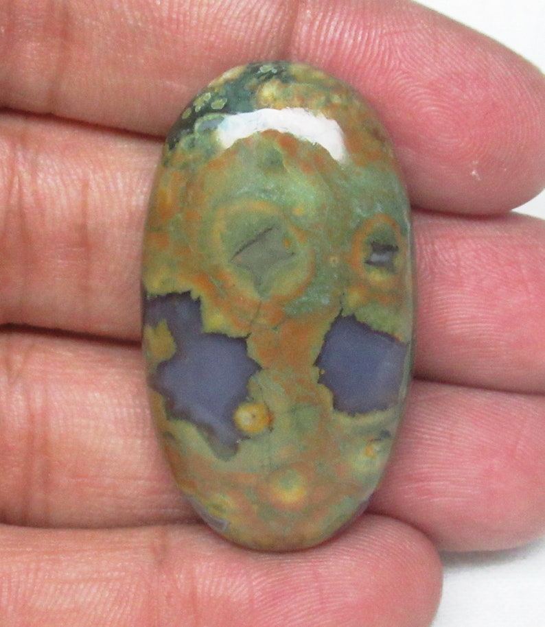 May include: A green, brown, and purple oval-shaped cabochon gemstone with a unique pattern of swirls and spots.
