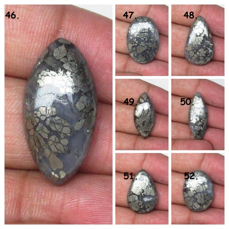 May include: A collection of six cabochon cut, silver and gray, pyrite stones. The stones are all different shapes and sizes, but they all have a similar pattern of pyrite inclusions.