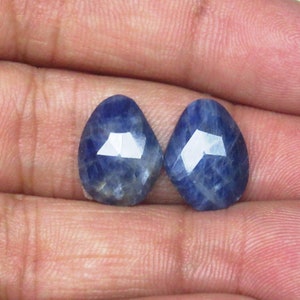 May include: Two blue gemstone cabochons with faceted edges. The stones are pear-shaped and have a light blue color.