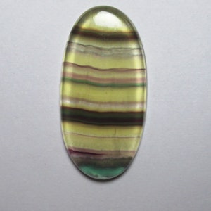 Puede incluir: Una piedra preciosa ovalada en cabuj&oacute;n con bandas verdes, amarillas y moradas. La piedra est&aacute; pulida y tiene un acabado liso y brillante.