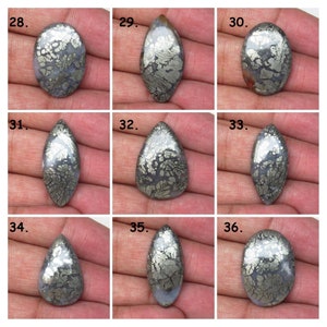 May include: Nine cabochon gemstone cabochons with a silver and gray marbled pattern. The cabochons are arranged in three rows of three. The cabochons are all different shapes and sizes.