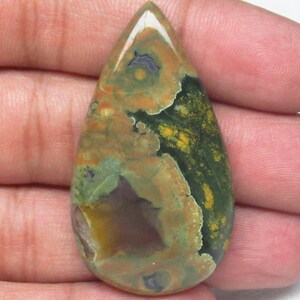 May include: A teardrop-shaped green, brown, and yellow gemstone cabochon with a mottled pattern.